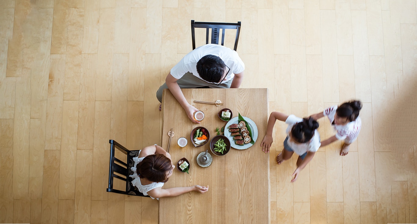 親子四人の家族写真。食事がテーブルに載っており、親が着席している様子を真上から移している写真。