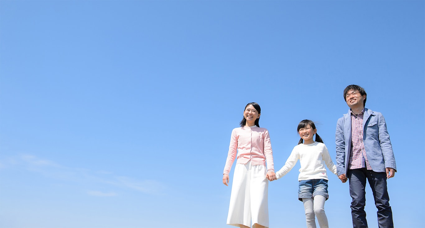 親子三人の家族写真。青空を背景に、子供を真ん中にして、三人で手をつないでいる。